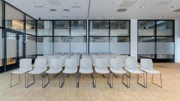 A conference room with rows of white chairs, large windows, and a wooden floor.