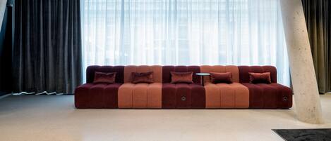 A modern living area with a sofa, a round table, and a large window with sheer curtains.