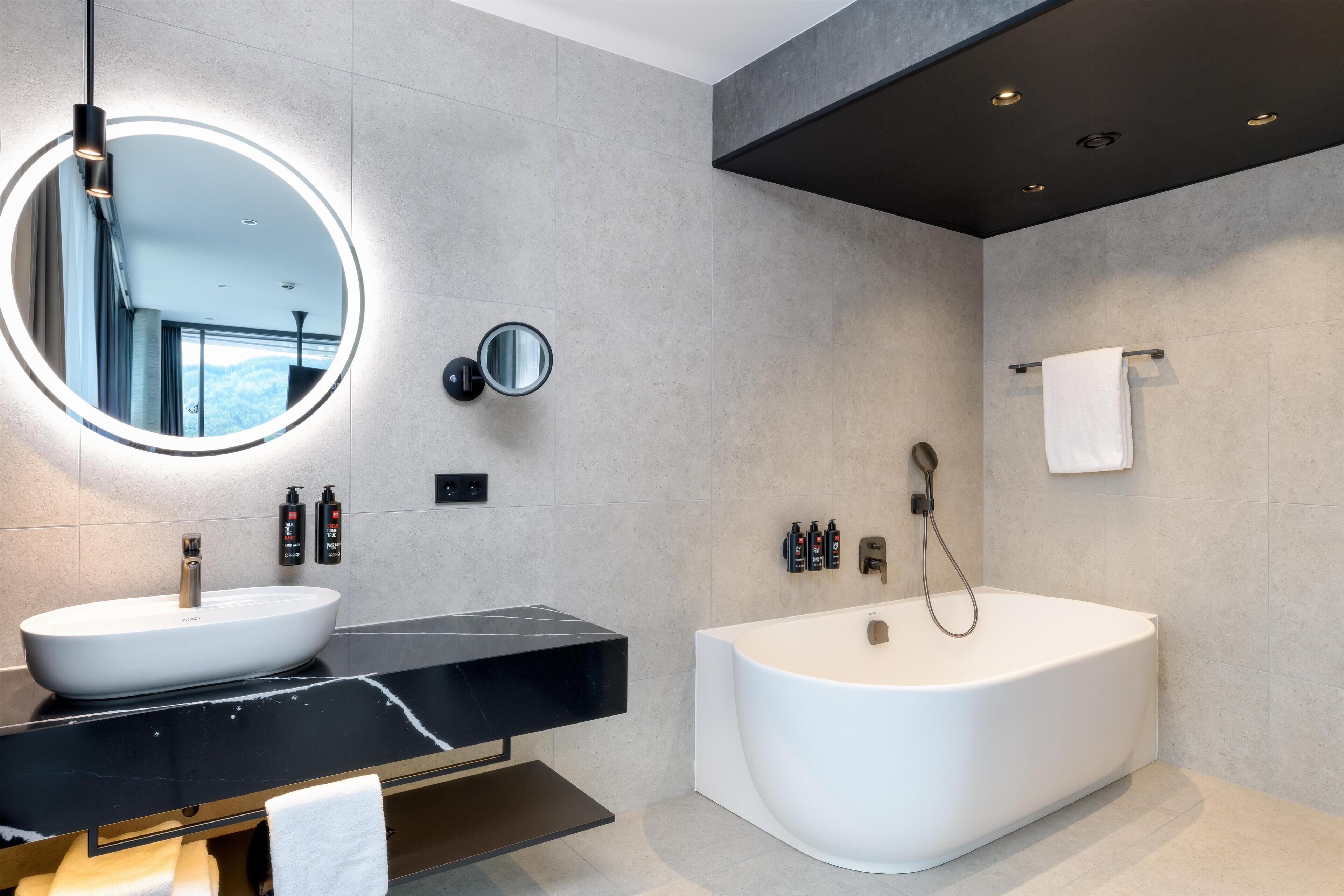A modern bathroom with a round mirror, two sinks, a bathtub, and a towel rack.