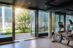 A gym with exercise equipment and large windows offering a view of greenery and buildings. - Radisson Red Innsbruck (Innsbruck)