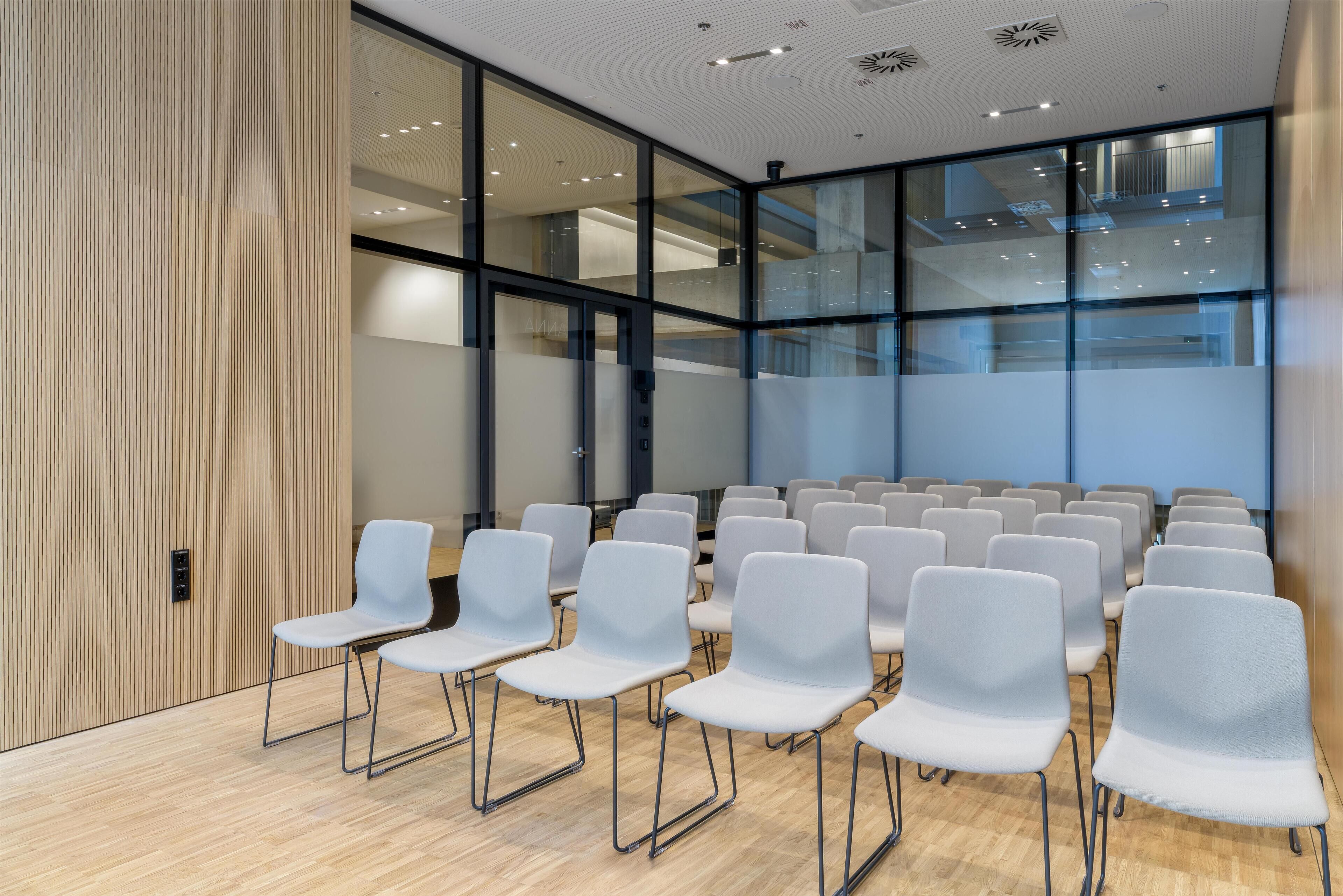 Ein Konferenzraum mit Stuhlreihen, großen Fenstern und einem modernen Deckenstil.