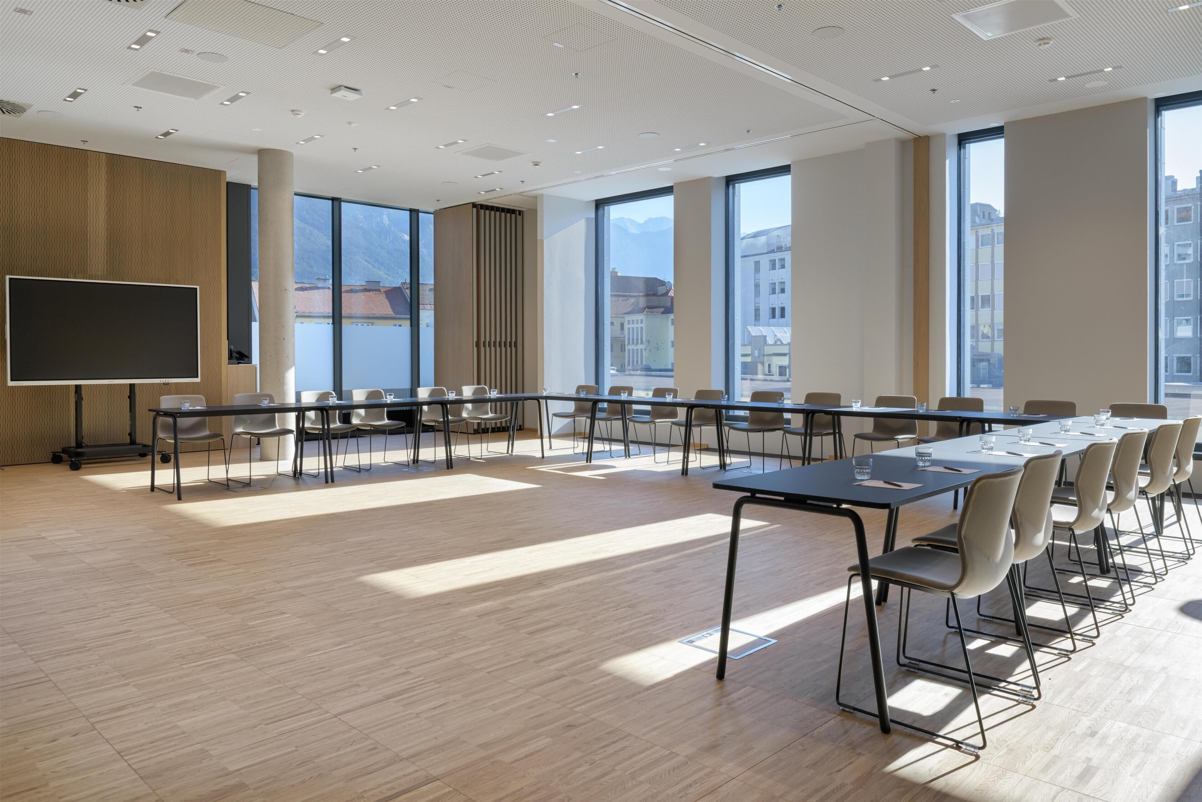 A conference room with a large table, chairs, a screen, and large windows with a city view.