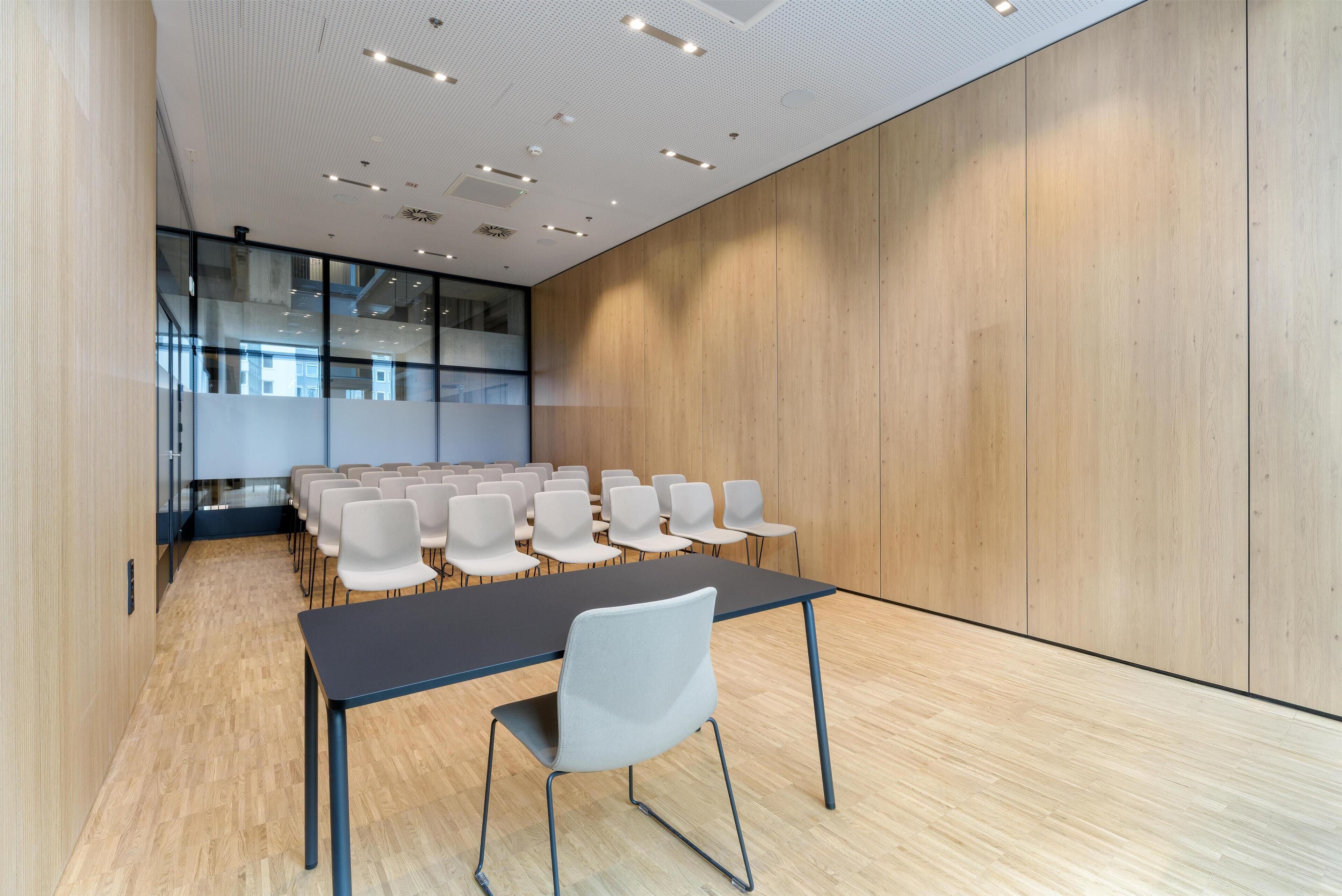 Un salón de conferencias con una larga mesa y sillas, paredes de madera e iluminación empotrada en el techo.