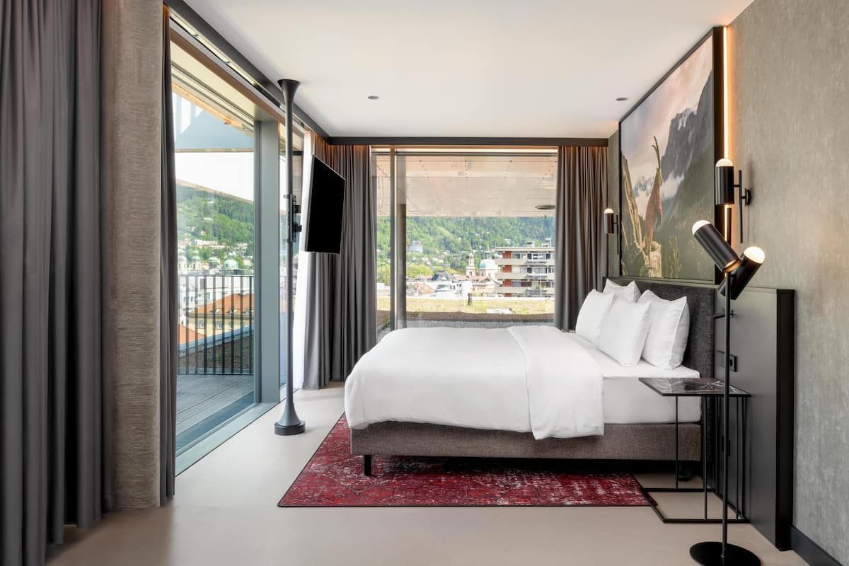 Ein modernes Hotelzimmer mit einem großen Bett, einem Fernseher, einem Schreibtisch und Blick auf die Stadt.