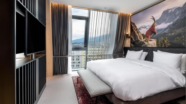 Une chambre d’hôtel moderne dotée d’un grand lit, d’une télévision à écran plat, d’un banc et offrant une vue sur la ville.