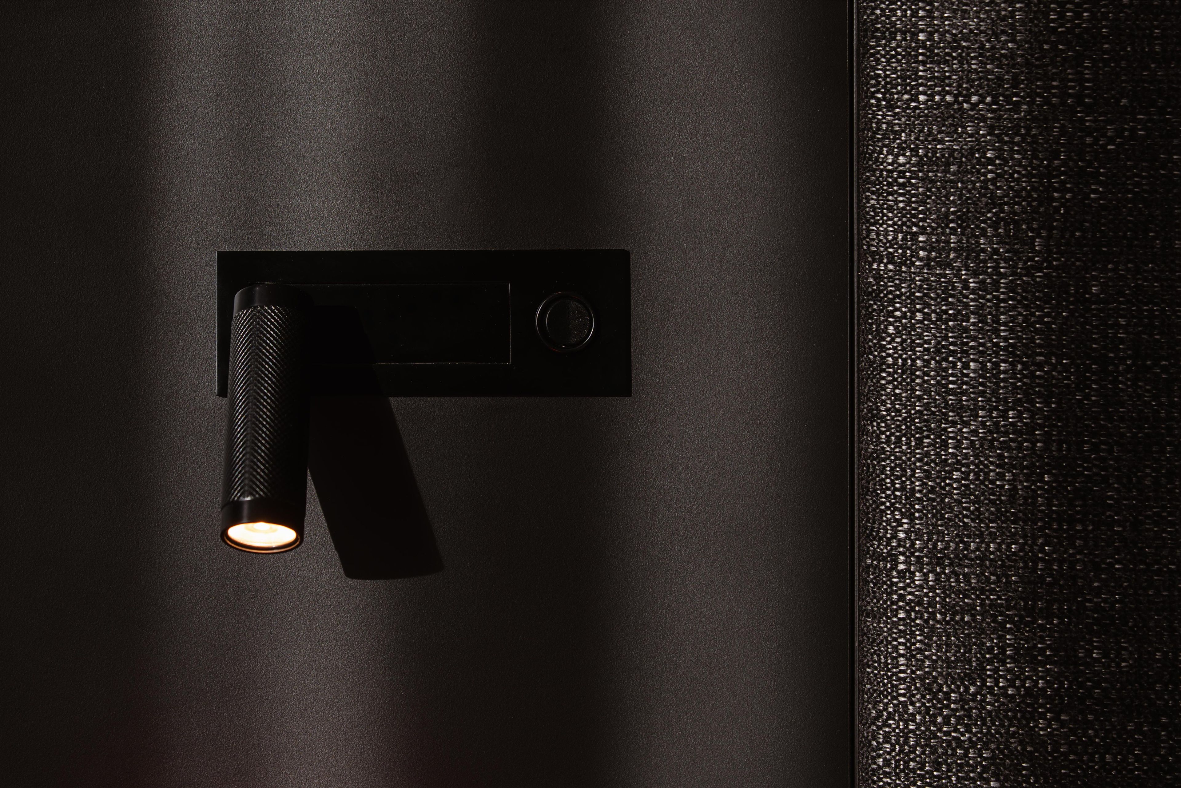 A modern, minimalist wall-mounted light fixture with a textured handle and a circular control dial.