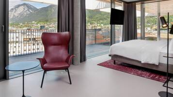Une chambre d’hôtel avec un lit, une chaise rouge, une petite table, un téléviseur et un balcon offrant une vue sur la montagne.