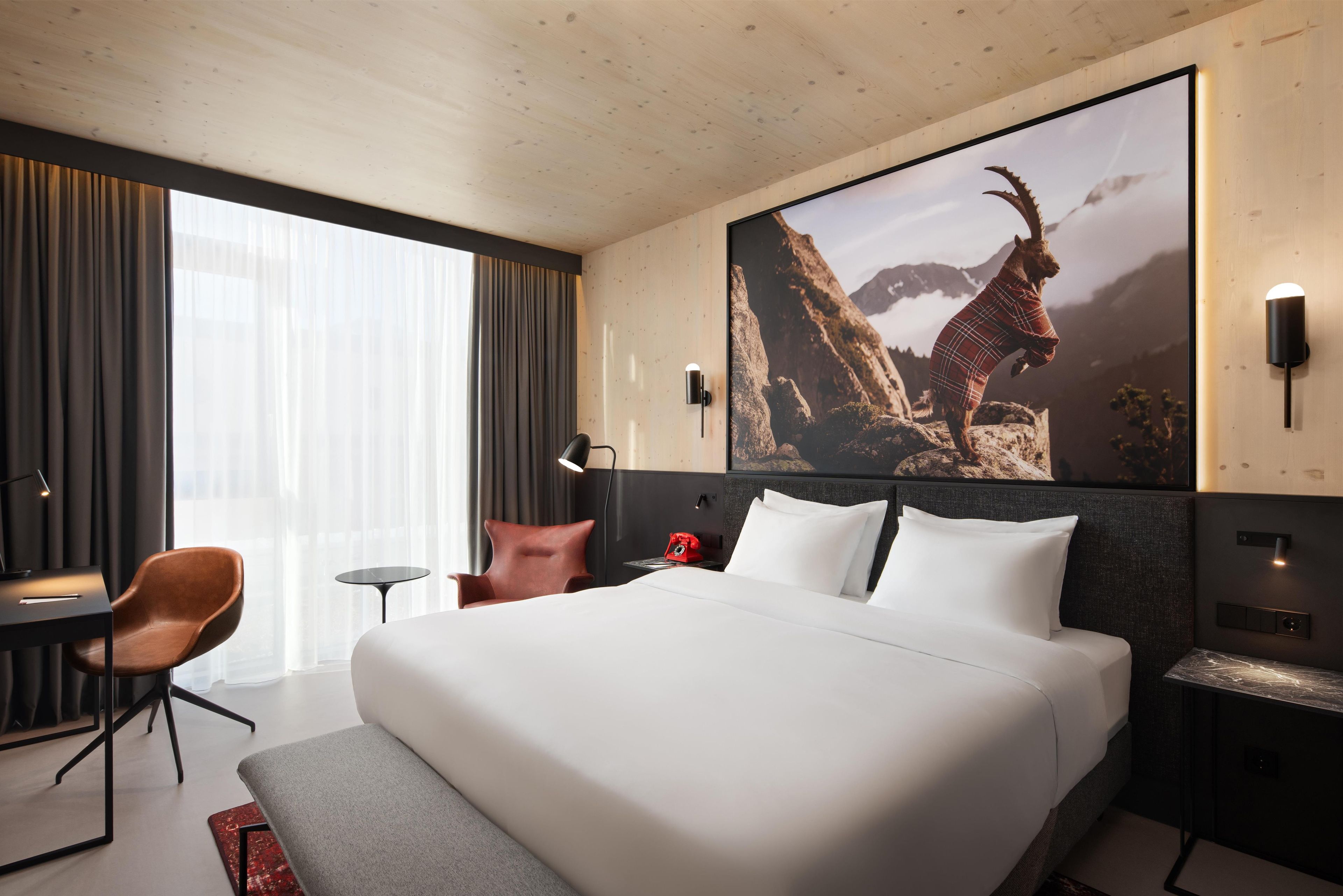 Ein Hotelzimmer mit einem großen Bett, einem Schreibtisch, einem Stuhl, einem Nachttisch und einem an der Wand befestigten Fernseher.