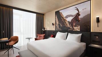 Ein Hotelzimmer mit einem großen Bett, einem Schreibtisch, einem Stuhl, einem Nachttisch und einem an der Wand befestigten Fernseher.