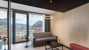 Une chambre moderne avec un canapé, une petite table, un banc et une grande fenêtre donnant sur une vue imprenable sur les montagnes.