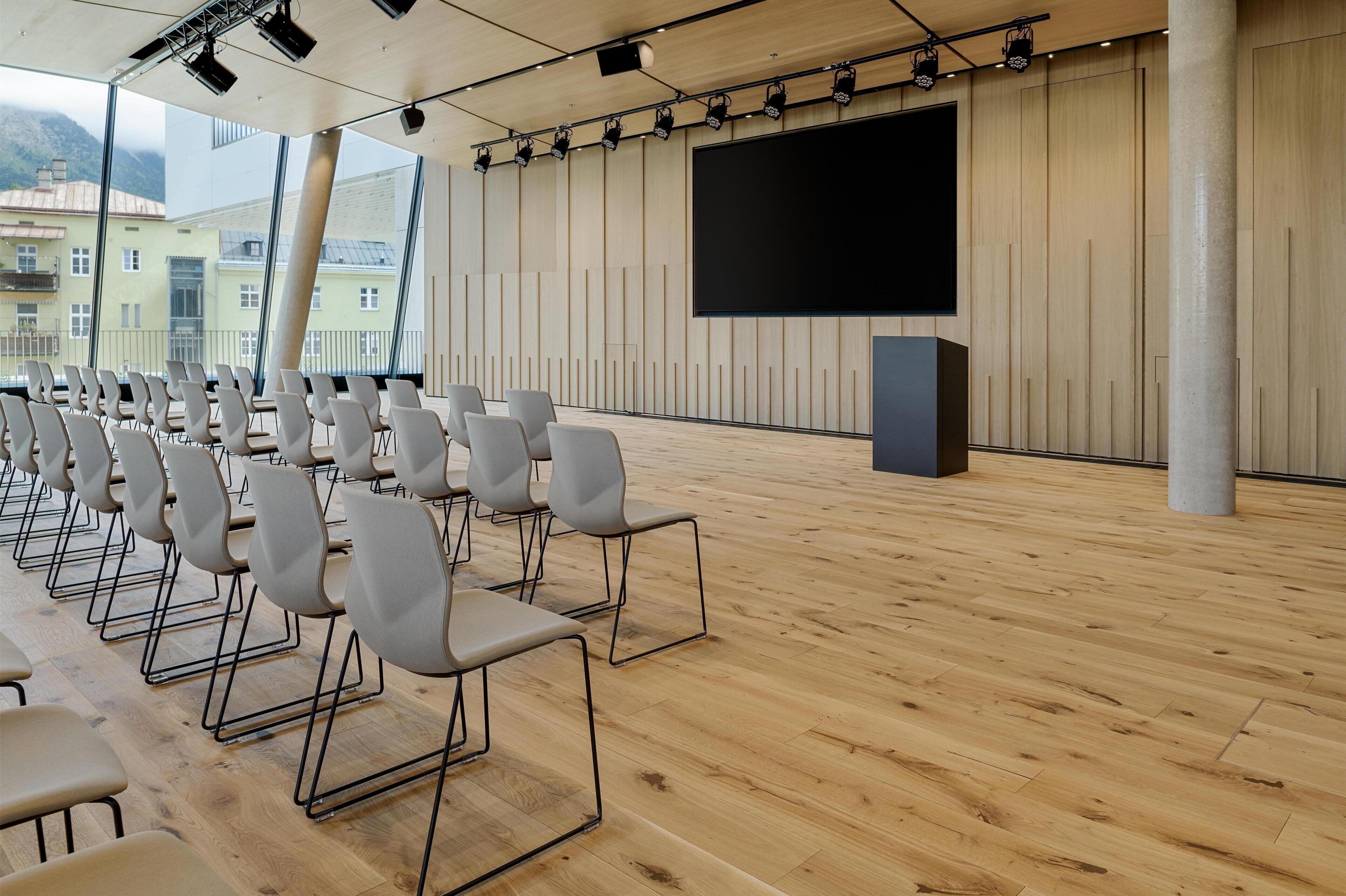 A conference room with rows of chairs, a large screen, and wooden paneling.