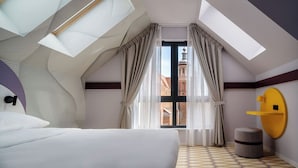 A modern hotel room with a skylight, a bed, a round yellow wall-mounted shelf, and a view of a building through the window.