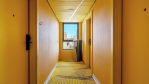A narrow hallway with yellow walls and a patterned floor, leading to a door with a window view of buildings.