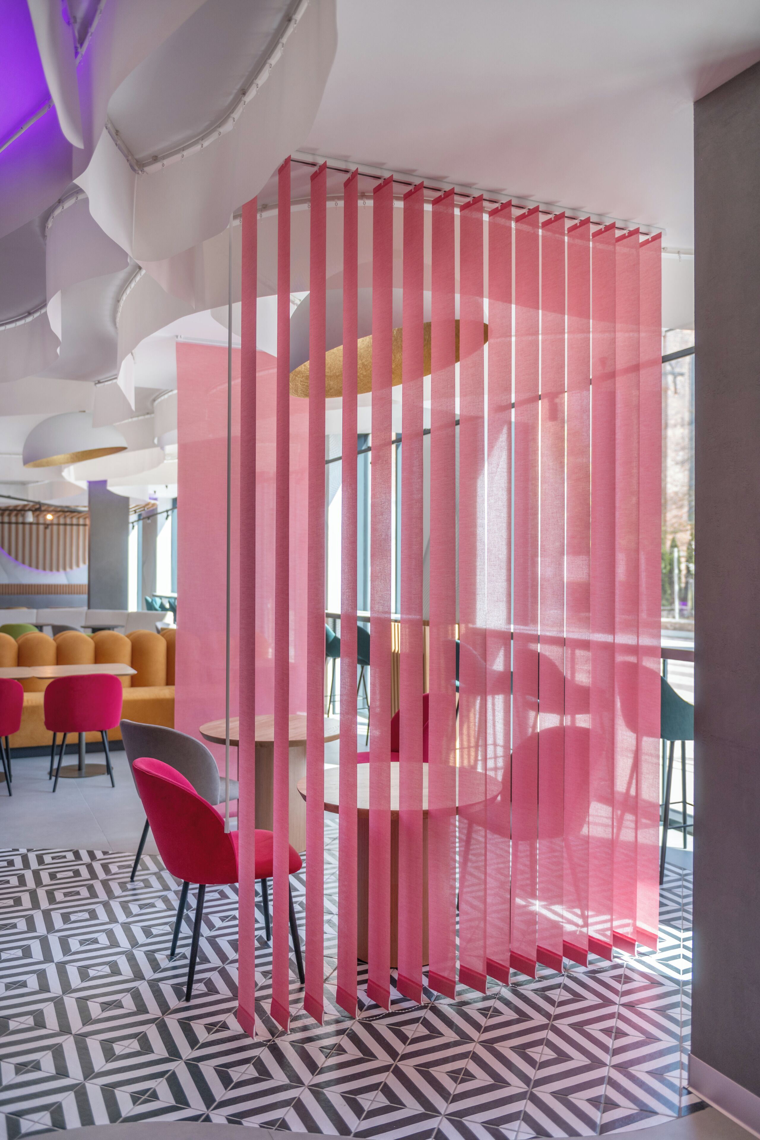 Un interior moderno con suelo de estampado geométrico, un área de estar con sillas naranja y rosa, y un separador con listones verticales.