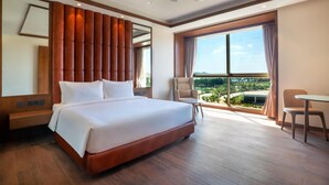 Habitación de hotel con una cama grande, ventilador de techo, vistas al exterior y un espacio para sentarse.