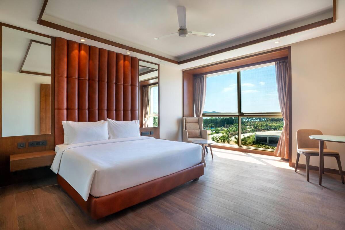 A hotel room with a large bed, a ceiling fan, a view of the outdoors, and a seating area.