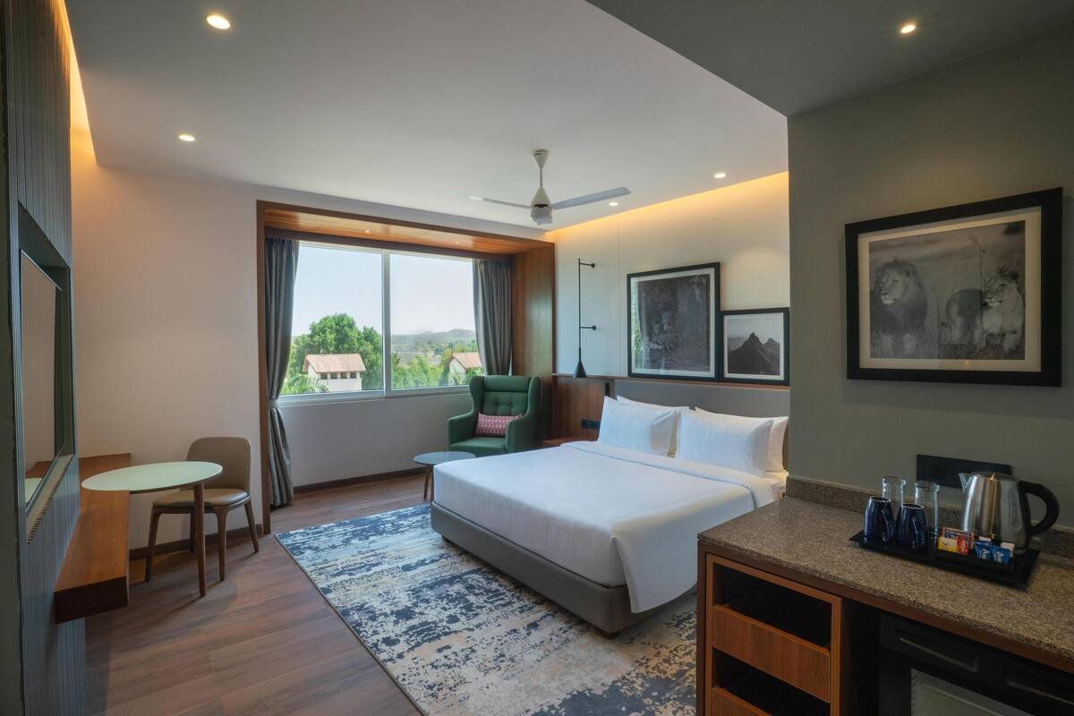 A hotel room with a bed, a desk, a chair, a coffee maker, and framed artwork on the walls.