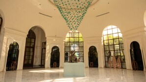 Un interior espacioso con ventanas arqueadas, una mesa central con una escultura y un techo con adornos colgantes.