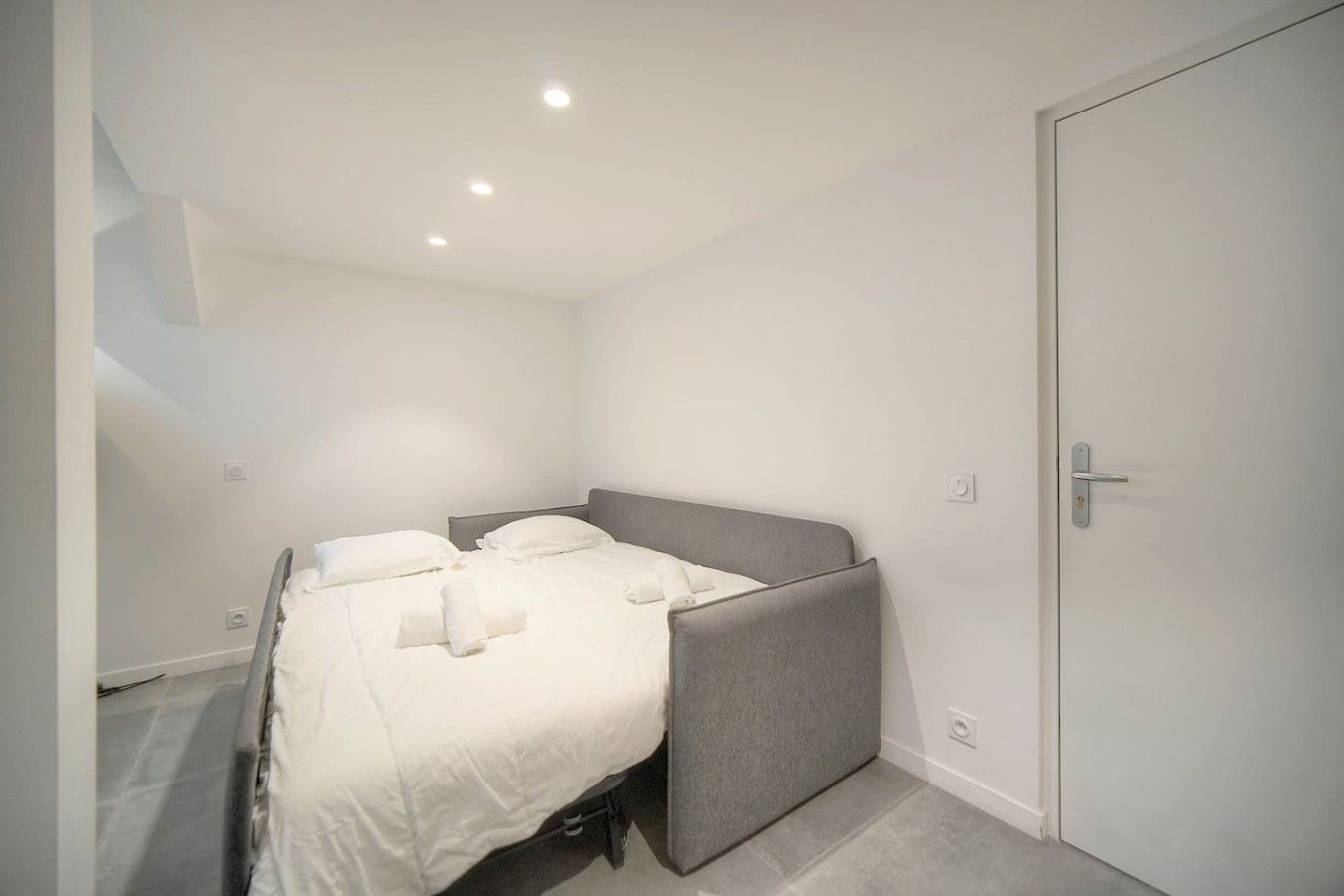 A single bed with a grey headboard in a room with white walls and a door.