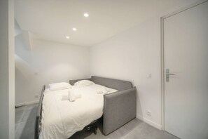 A single bed with a grey headboard in a room with white walls and a door. - Question 24. August, 2-room apartment in the center of Antibes, quiet location` (Antibes)