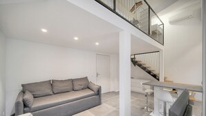Ein modernes Wohnzimmer mit grauem Sofa, einem Essbereich mit Bar und einer Treppe, die zu einer oberen Ebene führt.