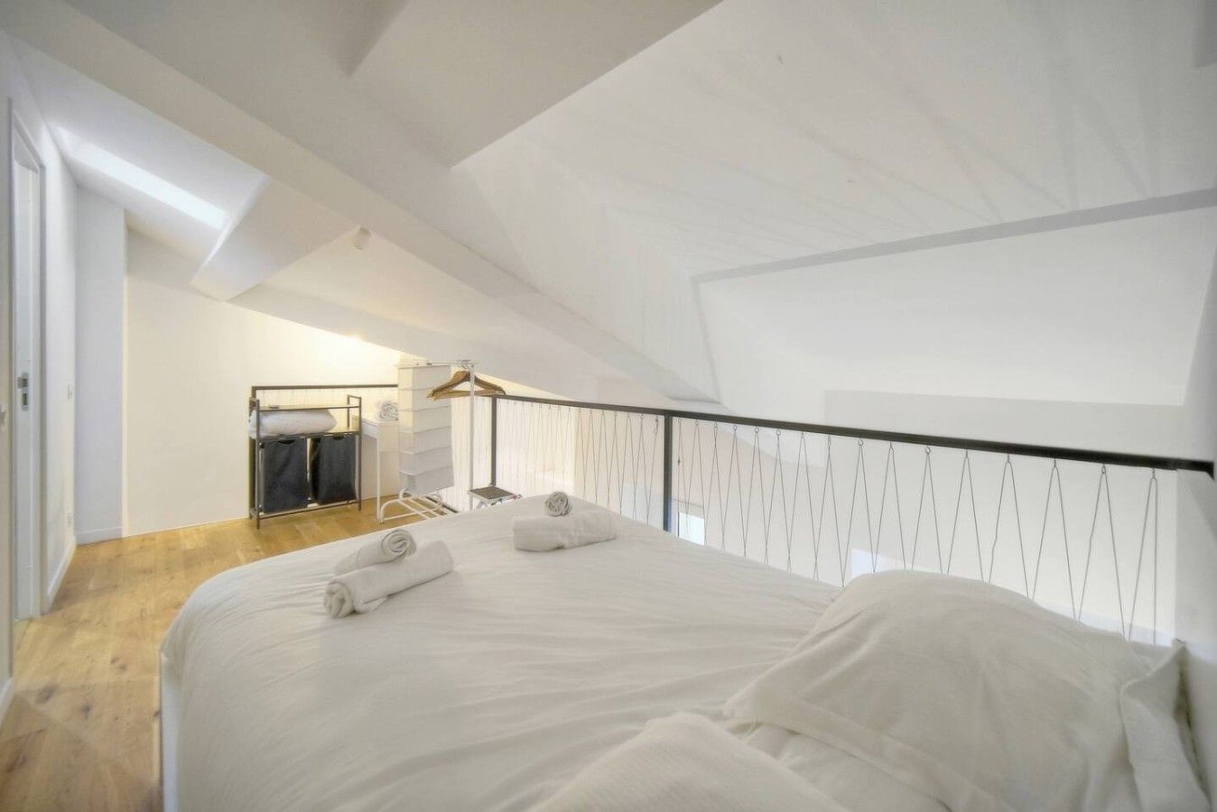 A bedroom with a large bed, a hanging light fixture, and a wooden floor.