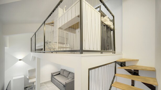 Ein modernes Interieur mit Treppe, einem grauen Sofa und einem weißen Schreibtisch.
