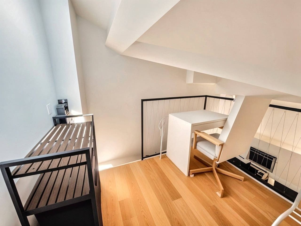 A modern, compact room with a wooden floor, a desk with a chair, and a small seating area.