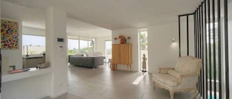 Amplia sala de estar con sofá, un mueble aparador y una silla. Un ventanal grande proporciona luz natural.