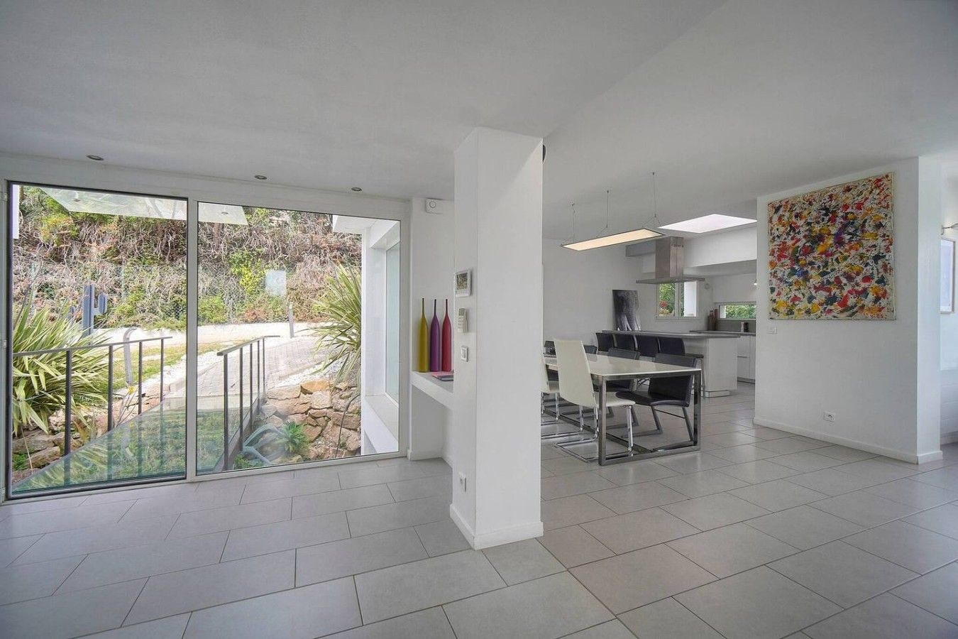 A spacious interior with a dining area, kitchen, and large windows offering a view of the outdoors.