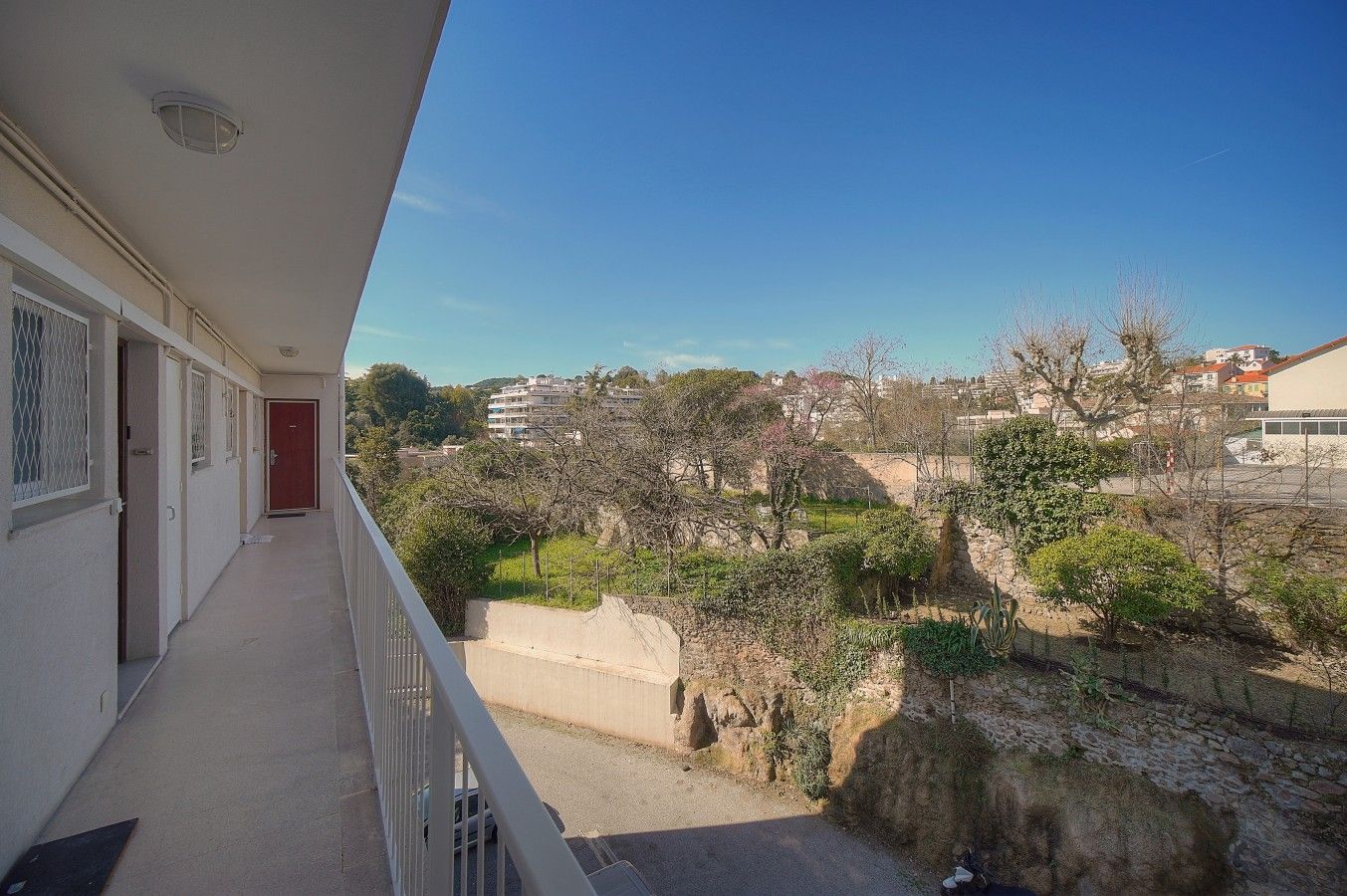A balcony with a view of a residential area, a stone wall, and a red door.