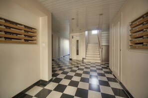 Ein Flur mit Schachbrettmuster-Boden, Holzschränken an den Wänden und einer Treppe, die zu einer anderen Ebene führt.