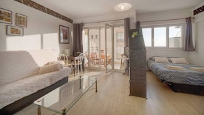 Ett modernt vardagsrum med en soffa, ett soffbord i glas, en säng och en matplats med stolar och ett bord.