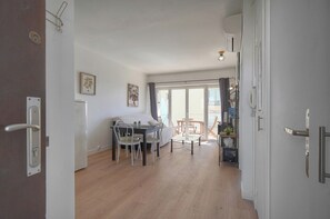 Ein geräumiger Wohnbereich mit Esstisch, Stühlen und einer Couch. Ein Balkon bietet einen Ausblick, und der Raum ist modern gestaltet, mit weißen Wänden und Holzböden.