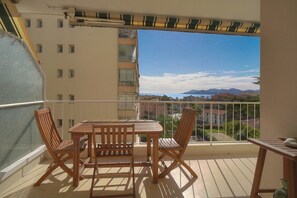 Ein Balkon mit Tisch und Stühlen, Blick auf Gebäude und Berge, und ein klarer Himmel.