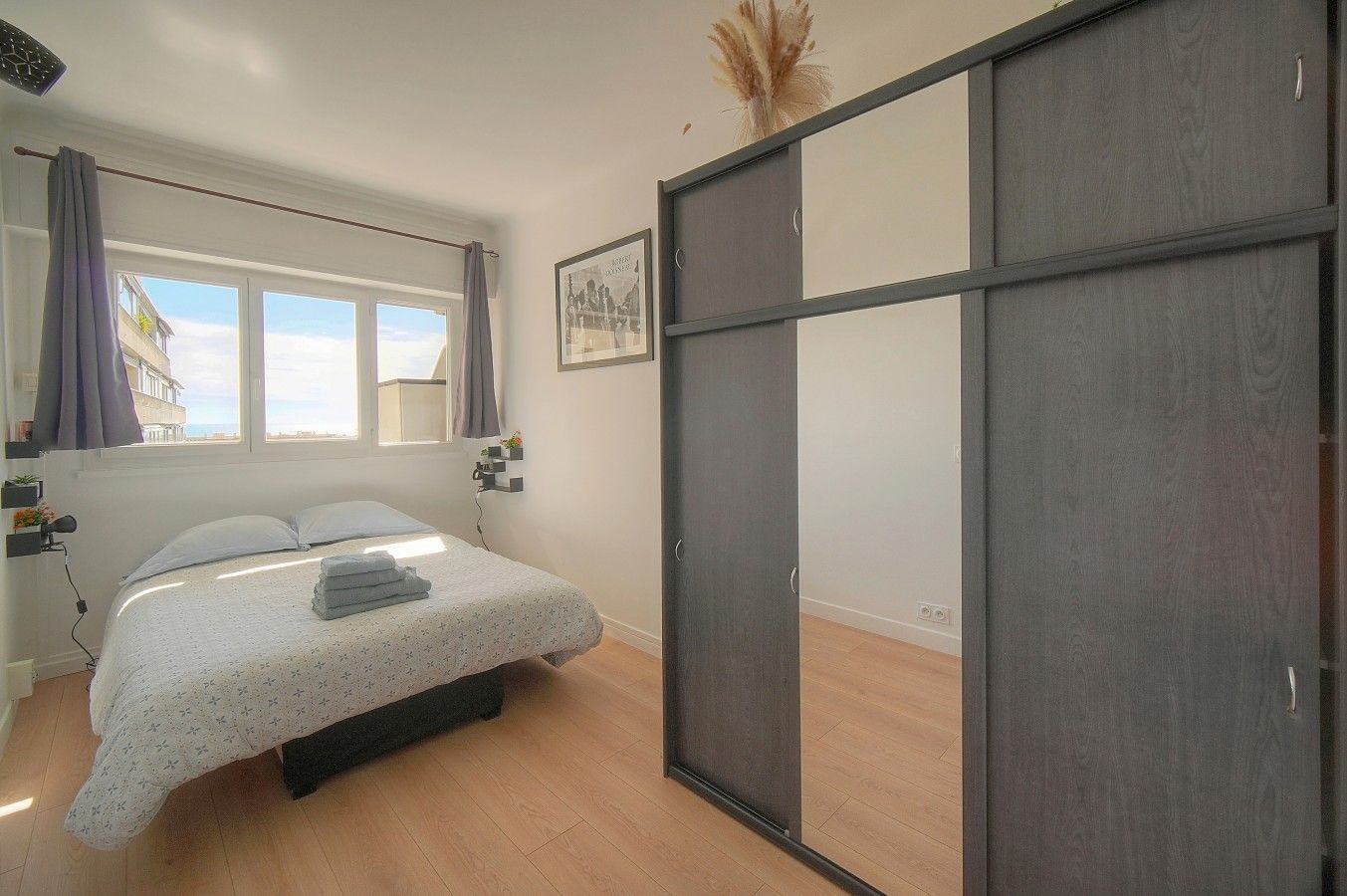 A bedroom with a bed, a wardrobe, a window with curtains, and a wall-mounted picture.