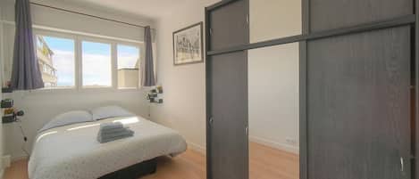 A bedroom with a bed, a wardrobe, a window with curtains, and a wall-mounted picture.