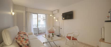 Un salon moderne avec un canapé, un fauteuil, une table basse et un téléviseur fixé au mur.