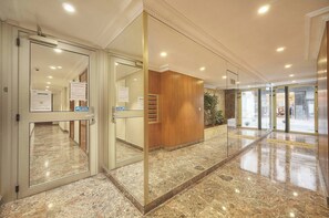 A hotel lobby with a marble floor, glass doors, a wooden reception desk, and a plant. - 13232804 FRGK Victoria 3 Central Cannes Studio Ter (Cannes)