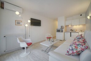 A compact living space with a kitchenette, a flat-screen TV, a dining table, and a sofa with a floral pillow. - One-bedroom apartment in France, Cannes (Cannes)
