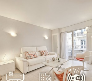 A modern living room with a white sofa, a coffee table, and a view of the city through large windows. - 13232804 FRGK Victoria 3 Central Cannes Studio Ter (Cannes)