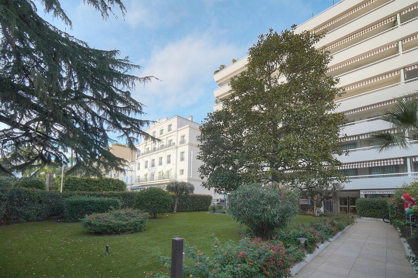A hotel courtyard with a well-maintained lawn, a variety of shrubs, and a pathway leading to the entrance.