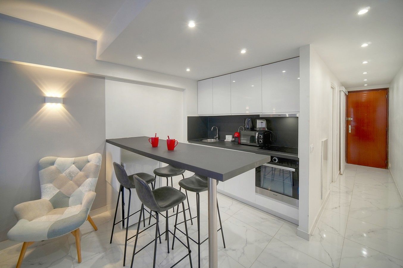 Una cucina moderna con angolo bar, mobili bianchi e un bollitore rosso.