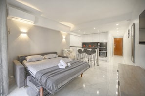 Ein modernes Hotelzimmer mit Bett, einer kleinen Küchenzeile und einer Sitzecke mit Stühlen.