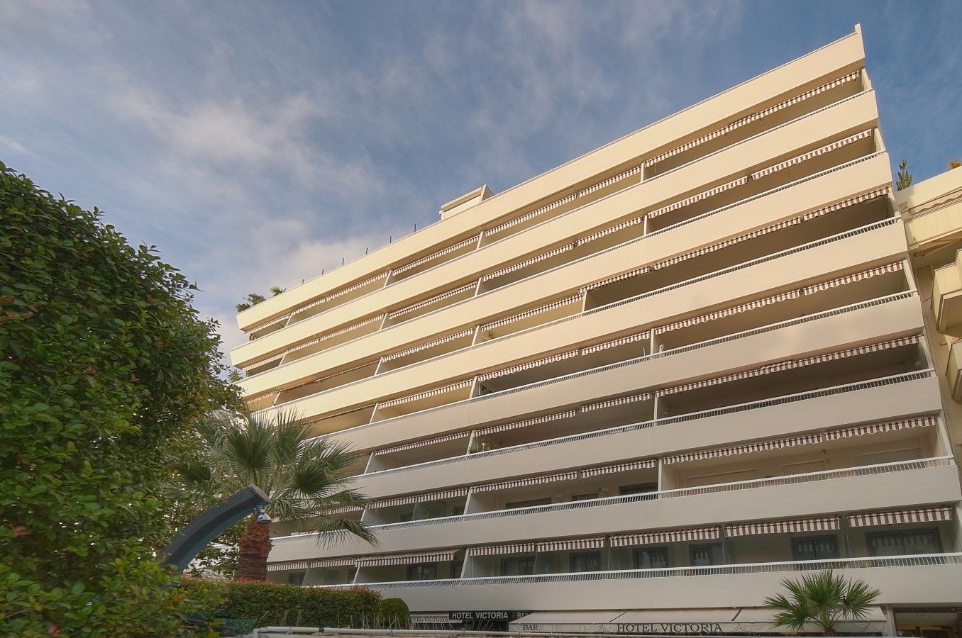 Un hotel a più piani con balconi su ogni piano, un bar e una zona piscina.