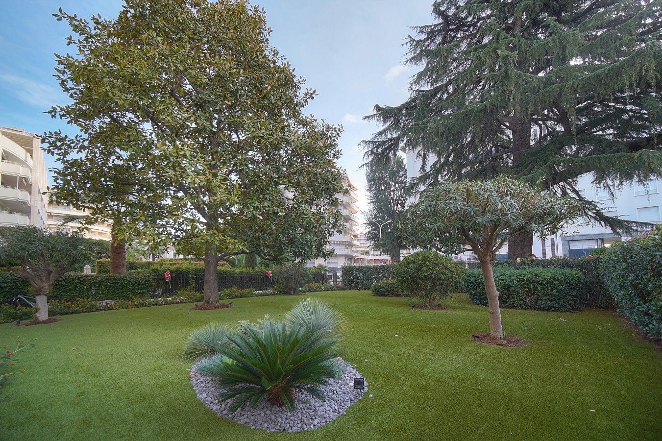 A well-maintained garden with various trees and shrubs, a neatly trimmed lawn, and a circular plant bed in the center.
