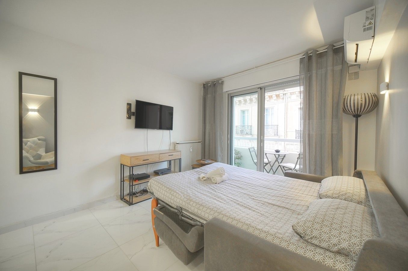 Una camera d'hotel moderna con un letto, una TV, una scrivania e un balcone con vista.