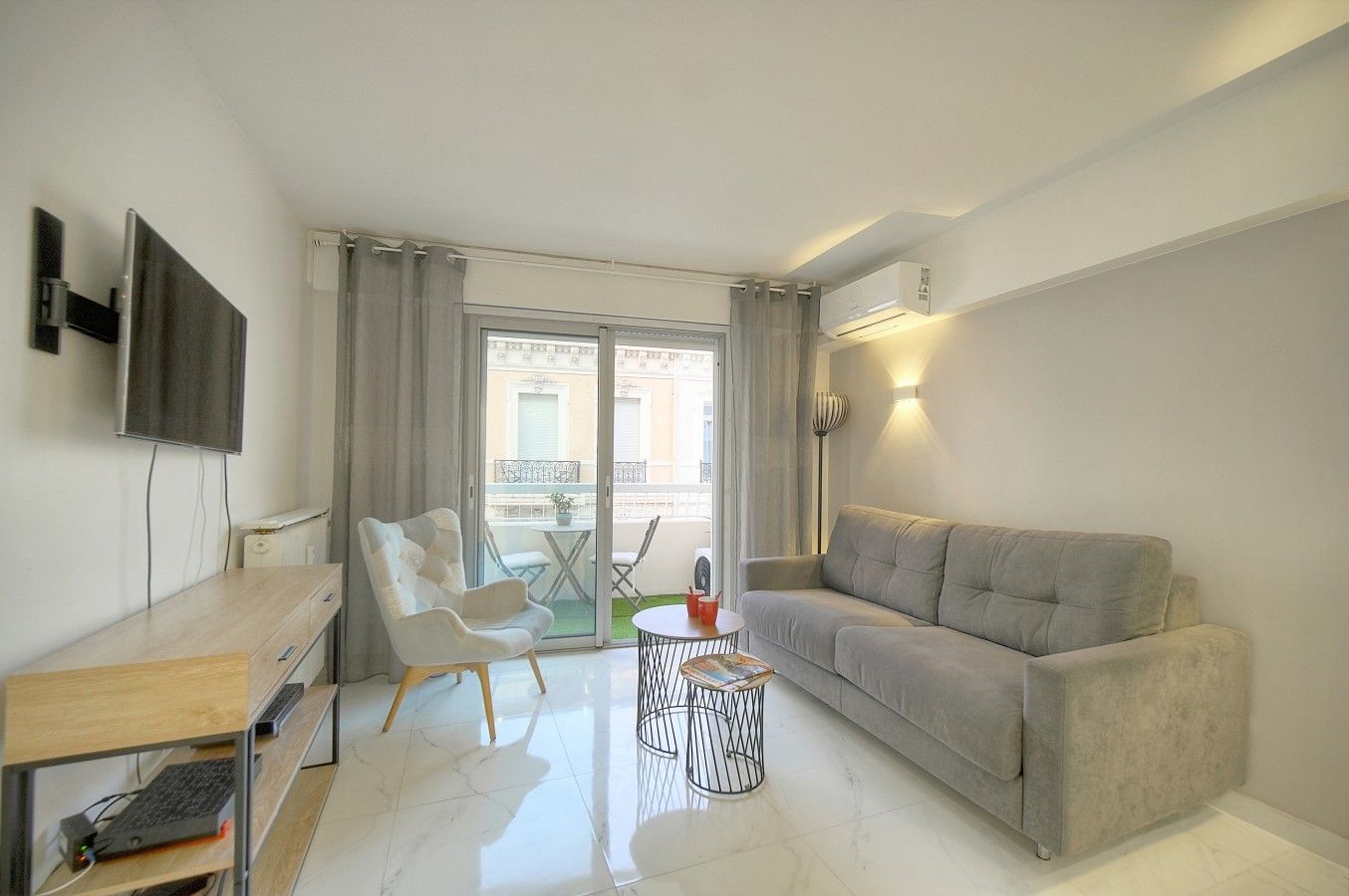 A modern living room with a sofa, a chair, a small table, and a TV mounted on the wall.