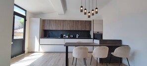 Eine moderne Küche mit Essbereich, Holzschränken, einer schwarzen Arbeitsplatte und Pendelleuchten.