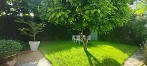 Un jardin bien entretenu, avec une pelouse, un arbre, ainsi qu’une table et des chaises blanches destinées à l’extérieur.